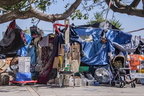 Boxes, prams, tarps, and other disparate items piled up under a blue sky on the sidewalk