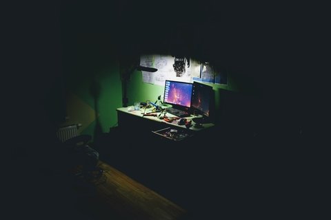 Two computer screens on a desk in a dark room. The light is focused on the computers