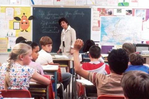 A teacher looking at a classroom of students, with one student's hand in the air