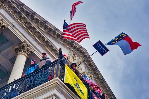 A U.S Flag, A Trump and Pence flag and other flags flying from the balcony of the Capitol building.