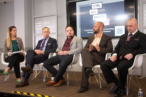 A white woman and four men sitting in chairs in straight line. Behind them a board says "Ctrl Alt Delete Hate".