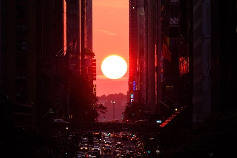 A sunset between buildings and a road full of vehicles.