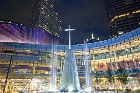 Modern, glass building with large cross sculpture in front surrounded by large fountain.