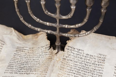 Old scrolls of the Bible and Menorah lie on a black background.