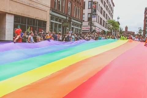 Group of people holding large pride flag above street at pride parade.