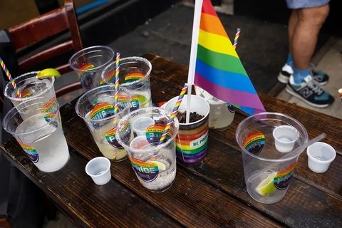 Plastic glasses with rainbow decals that say "Pride" on a table with remnants of drinks and a rainbow flag.