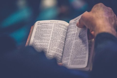 Person's hand turning a page of a Bible.