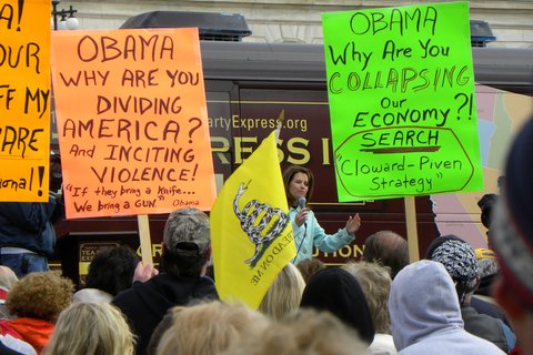 Protesters with signs that say "Obama why are you dividing America? And inciting violence!" and "Obama Why are you collapsing our economy?"