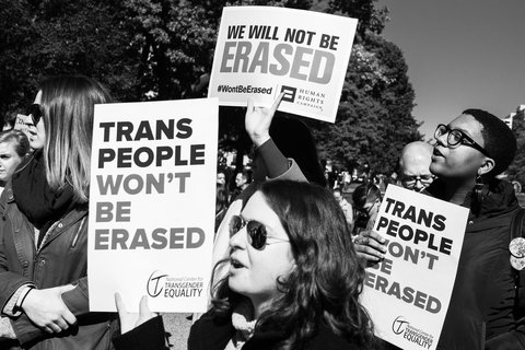People at a protest holding signs that say "Trans people will not be erased" and "we will not be erased"