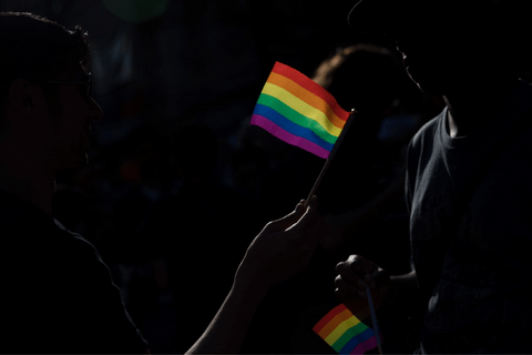 A dark image with silhouettes of hands, holding bright rainbow flags