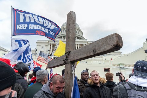The U.S. Capitol with a wooden cross in front of it and a Trump flag.