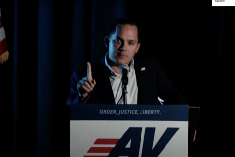 A man standing behind a podium with the American Virtue logo on it.