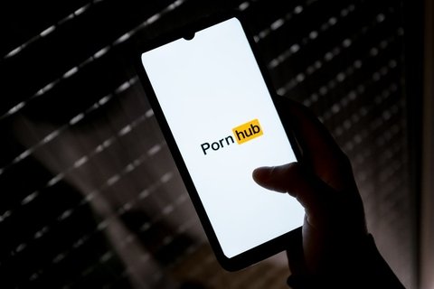 A hand on an illuminated phone with the logo of PornHub on it.