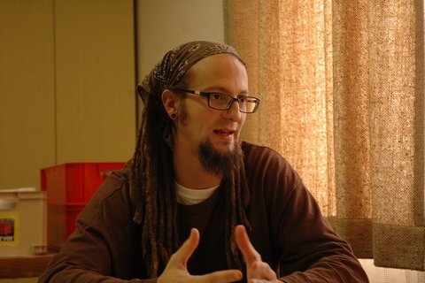 A White man wearing a sweater, with glasses and a bandana and dreadlocks.
