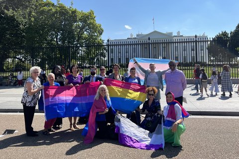 A group of people holding trans flags and bisexuality flags outside the White House.