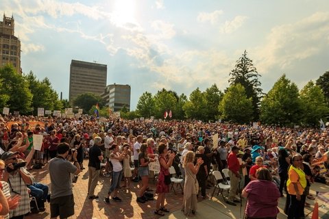 Protesters in a park with buildings in the background.