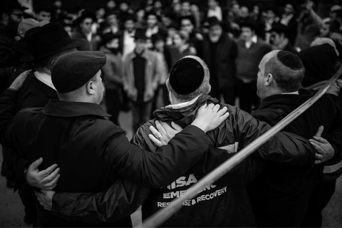 Three men in kippahs embracing in front of the Tree of Life memorial.