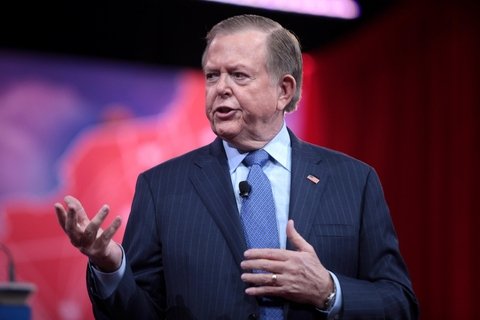 A man in a blue suit, speaking.