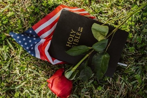 An american flag and a bible and a rose in a field