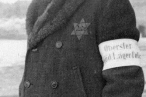 A man in a coat with the star of david, wearing a white arm band
