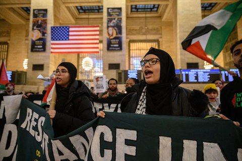 Two women in hijabs holding a protest sign.