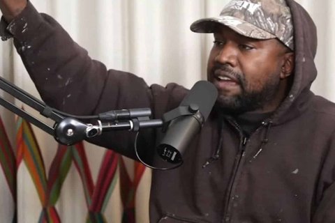 a black man wearing a hat and a hoodie speaking into a mic.