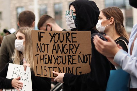 A person holding a sign that says "If you're not angry, then you're not listening."