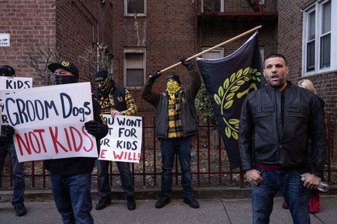 Proud Boys standing in a line holding anti-trans protest signs.
