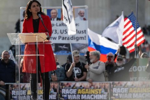 A woman with brown hair wearing a red coat speaking into a mic
