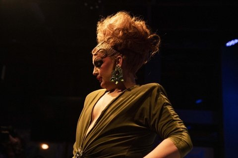 A Drag artist on stage, with yellow lighting on her. 
