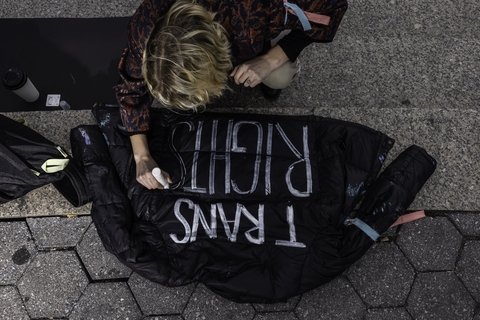 a person bending over writing the words "Trans Rights" on a black jacket.