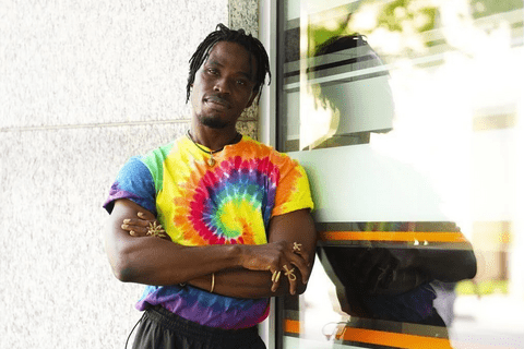 A black man wearing a tie-dye rainbow colored t-shirt.