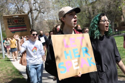 A person in a baseball hate holding a sign that reads "Let her speak."