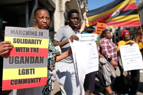 A woman in the front of the frame holding a sign that reads "marching in solidarity with the Ugandan LGBTI Community"