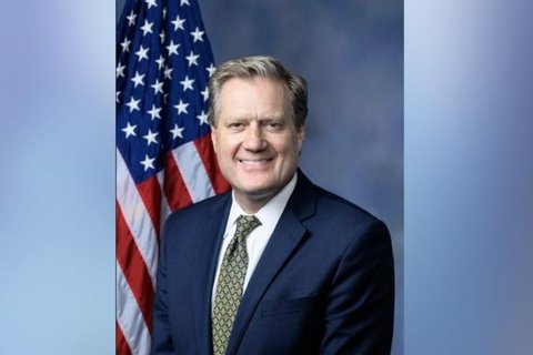 a man in a suit standing in front of the American flag.