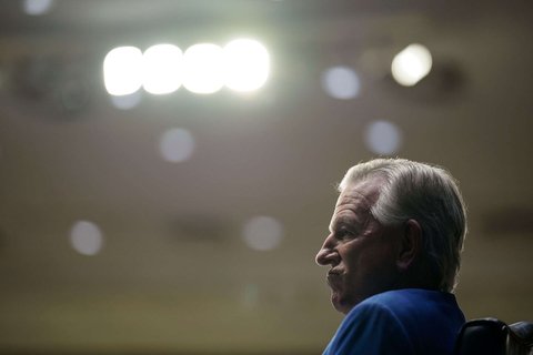 The profile of a white man sitting in a chair.