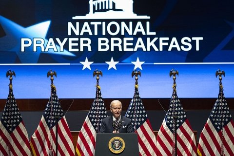 Joe Biden standing in front of a projected image that says "National Prayer Breakfast"