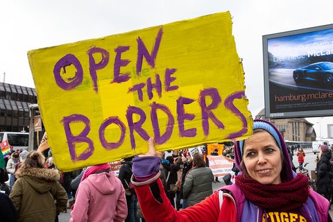A woman with a scarf holding a sign that says "open the borders"