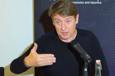 a man in a black t shirt talking into a mic