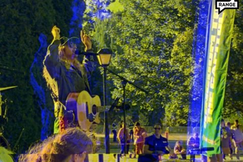 a man in a hat and a jacket with long hair speaking into a mic