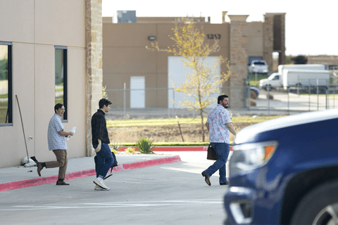 Nick Fuentes walking in front of a building with one person behind him and one person behind him.