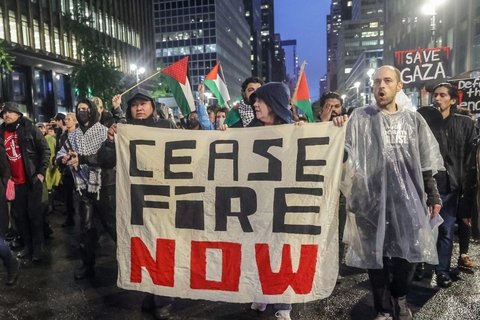 Protesters holding a sign saying "cease fire now"