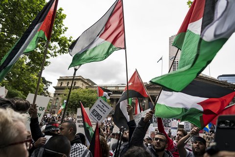 People protesting, waving red, white, and green Palestine flags in the air.