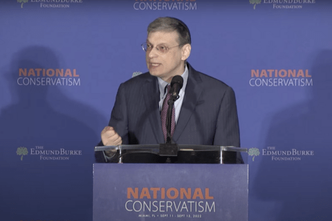 A Man in spectacles with greying hair talking at a podium that says "National Conservatism"