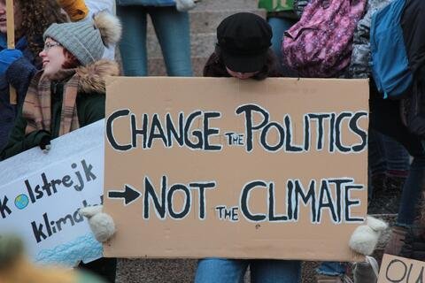 a protester with a sign that says "change the politics not the climate"