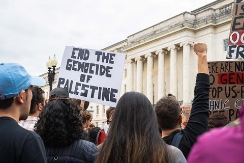 A protest with someone holding a sign that says "End the Genocide of Palestine"