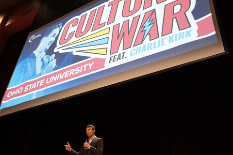 Charlie Kirk standing under a projection that says "culture war"