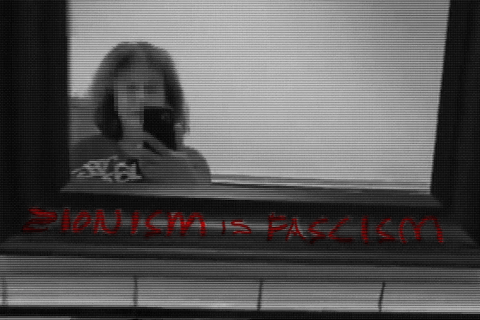 a person taking a picture of a mirror with graffiti on it that says "Zionism is fascism"