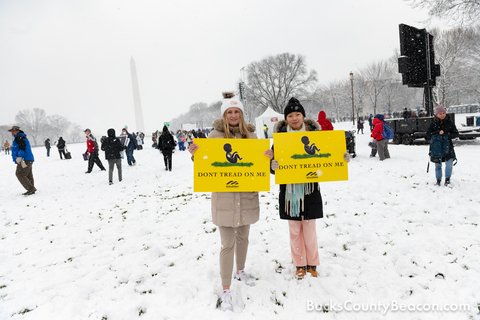 two women in winter wear holding signs that have a baby on grass that read "Don't Tread on me"
