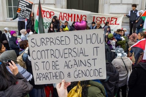 A Protestor holding a sign that says "Surprised by how controversial it is to be against Apartheid and Genocide"